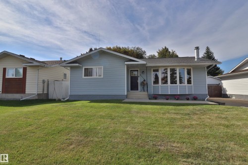 Light blue siding exterior with a dark gray front door, a prominent bay window, a concrete walkway, and a spacious green lawn - 4113 - 42 B Ave, Leduc, AB 