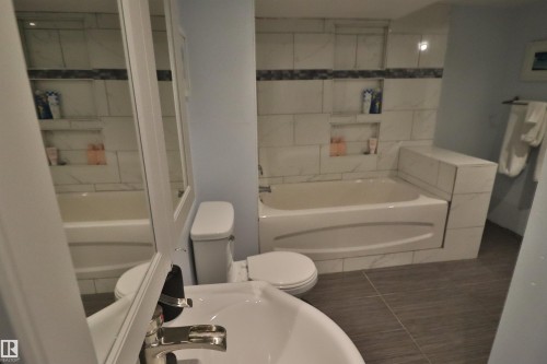 White subway tile shower surround with two integrated niches, bathtub with tiled enclosure, and a chrome faucet - 4113 - 42 B Ave, Leduc, AB 