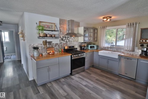 Kitchen featuring wood-finish flooring, gray cabinetry, wood countertops, a farmhouse sink, and stainless steel appliances - 4113 - 42 B Ave, Leduc, AB 
