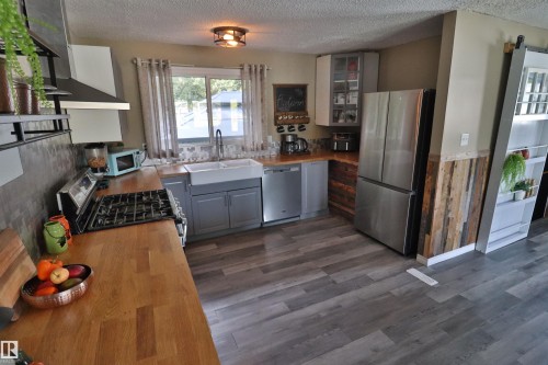 Kitchen featuring wood-finish flooring, butcher block countertops, white farmhouse sink, stainless steel appliances, and a range hood - 4113 - 42 B Ave, Leduc, AB 