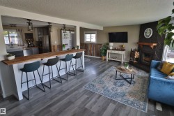 Open-concept living space featuring wood-finish flooring, a breakfast bar with a wood countertop, and a stone-clad fireplace with a wood mantel - 