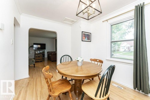 Wood-finish flooring throughout, framed window with sill, crown molding, archway opening, and a pendant light fixture - 10507 67 Avenue Nw, Edmonton, AB 