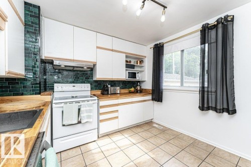 Kitchen featuring white cabinetry, wood-finish countertops, subway tile backsplash, and ceramic tile flooring - 10507 67 Avenue Nw, Edmonton, AB 