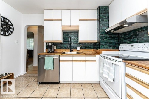 White cabinetry with wood-finish accents, wood-finish countertops, and a dark green tile backsplash - 10507 67 Avenue Nw, Edmonton, AB 
