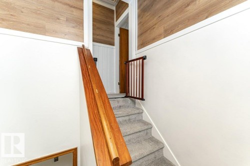 Carpeted staircase with a wood handrail, white wall paneling, and wood-finish wall accents - 10507 67 Avenue Nw, Edmonton, AB 