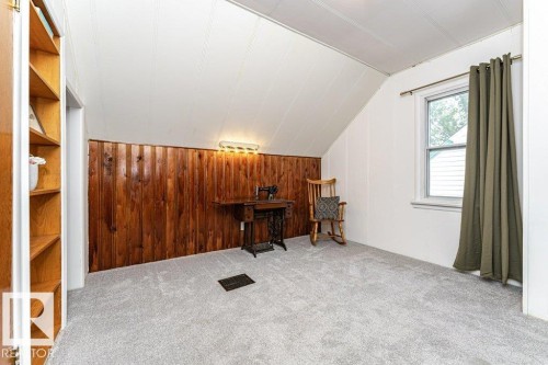 Built-in shelving unit, wood-paneled accent wall, wall-mounted lighting fixture, carpeted flooring, and a double-hung window - 10507 67 Avenue Nw, Edmonton, AB 