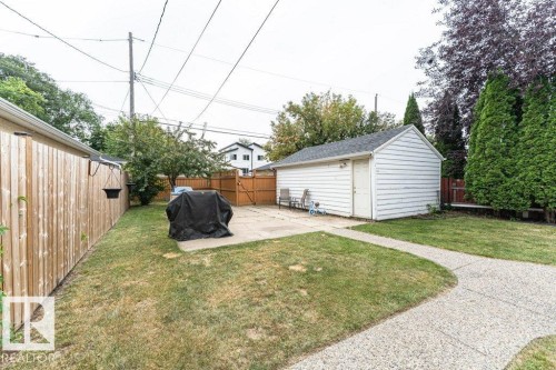 Detached garage with white siding, concrete patio, concrete pathway, wood fencing, and mature trees - 10507 67 Avenue Nw, Edmonton, AB 