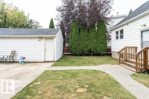Manicured lawn with concrete pathways, leading to a detached garage and a wood-decked entryway with railings - 10507 67 Avenue Nw, Edmonton, AB 