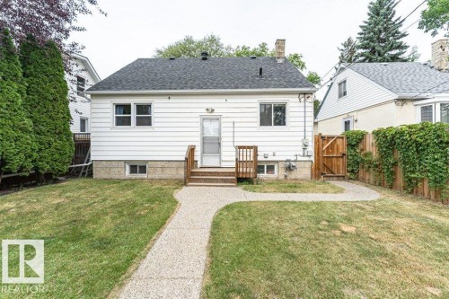 Expansive backyard featuring a manicured lawn, an exposed aggregate pathway, and a wooden privacy fence with an integrated gate - 10507 67 Avenue Nw, Edmonton, AB 