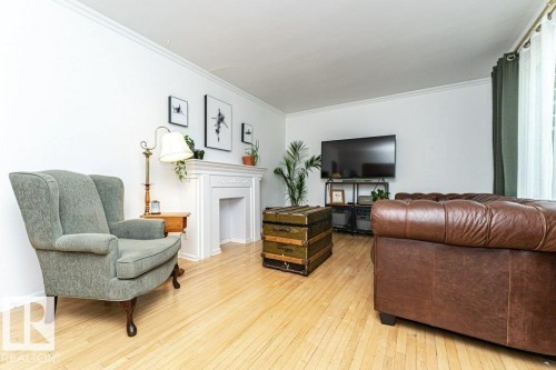 Crown molding with smooth white walls, light wood-finish flooring, white decorative fireplace surround, and a large window with sheer and opaque drapery - 10507 67 Avenue Nw, Edmonton, AB 