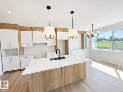 Modern kitchen featuring a large island with a waterfall countertop, white cabinetry with wood-finish accents, a subway tile backsplash, and light wood-finish flooring - 