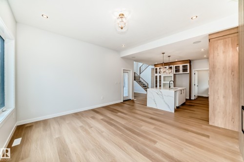 Wide plank wood-finish flooring, recessed lighting, kitchen island with waterfall countertop, dark wood-tone cabinetry, and a black metal staircase railing - 47 Meadowgrove Lane, Spruce Grove, AB 