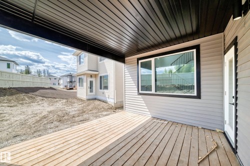 Covered outdoor patio with wood-finish decking, light gray siding, and a white trim window - 47 Meadowgrove Lane, Spruce Grove, AB 