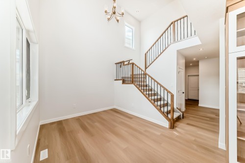 Two-story entry with a brass chandelier, wood-finish flooring, and white walls - 47 Meadowgrove Lane, Spruce Grove, AB 