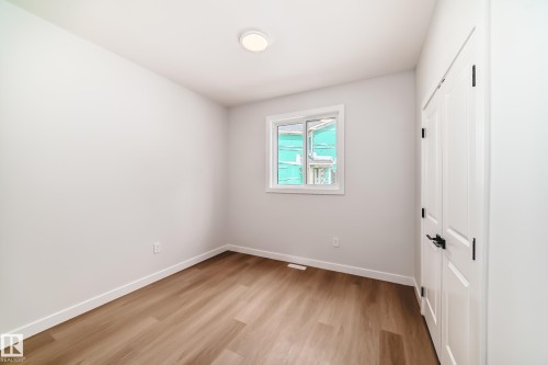 Wood-finish flooring with white baseboards, a single window, and a paneled door with dark hardware - 47 Meadowgrove Lane, Spruce Grove, AB 
