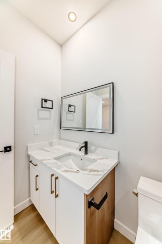 Modern vanity with integrated sink, white cabinetry with gold-tone pulls, a wood-finish side panel, and a matte black faucet - 47 Meadowgrove Lane, Spruce Grove, AB 