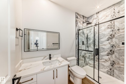 Modern bathroom featuring a single vanity with a white countertop and integrated sink, a large framed mirror, and a glass-enclosed shower with a black-framed sliding door - 47 Meadowgrove Lane, Spruce Grove, AB 