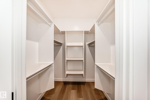 Built-in closet system featuring multiple shelves, hanging rods, and wood-finish flooring - 47 Meadowgrove Lane, Spruce Grove, AB 