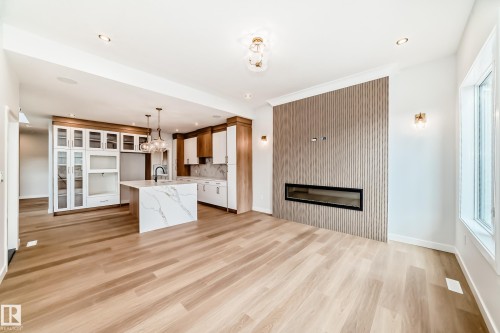 Wood-finish flooring throughout, kitchen with a large island and pendant lighting, built-in cabinetry, linear electric fireplace, and expansive windows - 47 Meadowgrove Lane, Spruce Grove, AB 