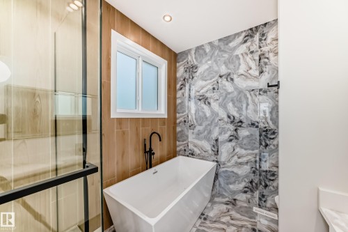 Freestanding soaking tub with matte black floor-mounted faucet, complemented by marbled wall and floor tiles - 47 Meadowgrove Lane, Spruce Grove, AB 