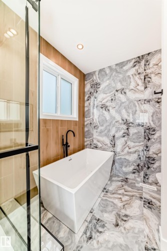 Freestanding soaking tub with a matte black floor-mounted faucet, set against wood-finish wall paneling - 47 Meadowgrove Lane, Spruce Grove, AB 
