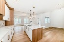 Gourmet kitchen featuring a central island with integrated sink, white cabinetry with gold-tone hardware, wood-finish flooring, and pendant lighting - 47 Meadowgrove Lane, Spruce Grove, AB 