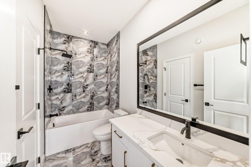 Bathroom featuring a white vanity with an integrated sink, a large framed mirror, and a tub-shower combination with patterned wall tile - 47 Meadowgrove Lane, Spruce Grove, AB 