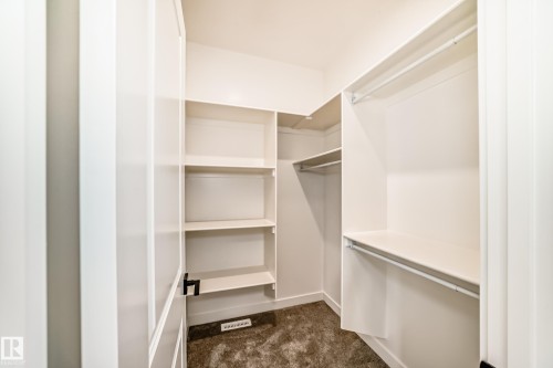 Walk-in closet featuring built-in shelving, multiple hanging rods, and carpet flooring - 47 Meadowgrove Lane, Spruce Grove, AB 