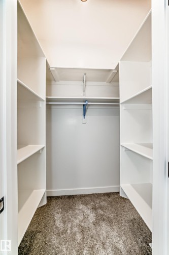 Recessed ceiling lighting illuminates a walk-in closet featuring white built-in shelving, a hanging rod, and carpet flooring - 47 Meadowgrove Lane, Spruce Grove, AB 