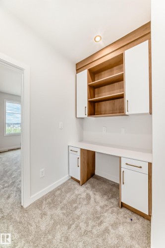 Built-in desk with a light-toned countertop, integrated shelving, and white cabinetry featuring gold-toned pulls - 47 Meadowgrove Lane, Spruce Grove, AB 