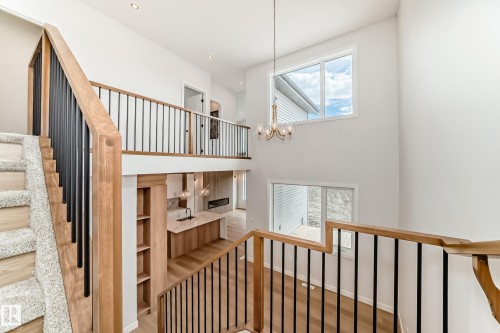 Two-story interior featuring wood-finish flooring, a contemporary chandelier, and a staircase with a wood handrail and black metal balusters - 47 Meadowgrove Lane, Spruce Grove, AB 