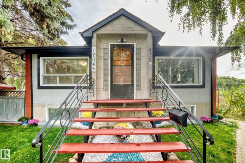 Exterior featuring a prominent red staircase with black metal railings, a central entry door, and two large front windows - 12045 64 Street Nw, Edmonton, AB 