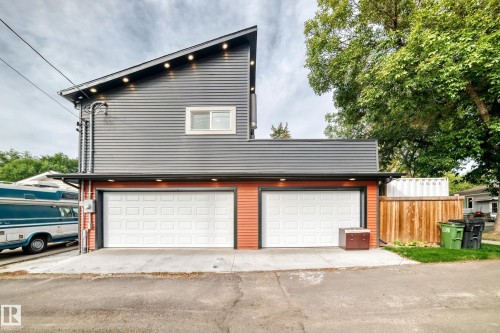 Modern two-story residence featuring a newly constructed garage with dual white panel doors, horizontal metal accents, and warm wood-finish fencing - 12045 64 Street Nw, Edmonton, AB 