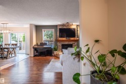 Wood-finish flooring throughout, featuring a stone-clad fireplace with a wood mantle, and a dining area with a linear chandelier - 