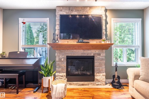 Stone-clad fireplace with a wood mantel, integrated television mount, and a black firebox - 38 Dubonnet Way, St. Albert, AB 