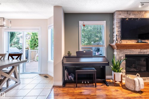 Stone-clad fireplace with wood mantel, built-in electric fireplace, wood-finish flooring, and sliding glass door leading to an outdoor deck - 38 Dubonnet Way, St. Albert, AB 