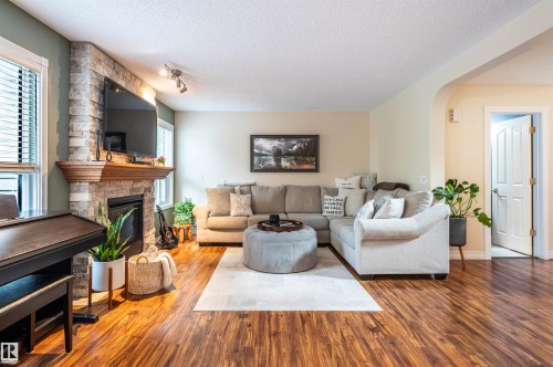 Stone-clad fireplace with a wood mantle, wood-finish flooring, and recessed archway - 38 Dubonnet Way, St. Albert, AB 