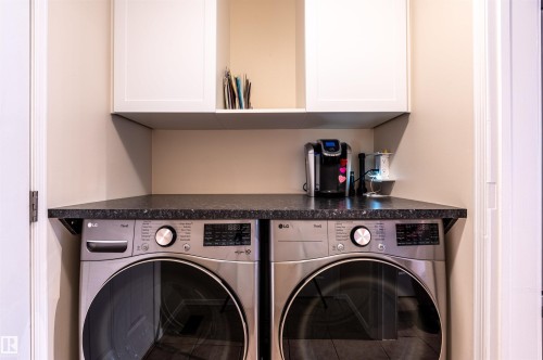 Integrated laundry appliances with a dark stone-finish countertop and white cabinetry - 38 Dubonnet Way, St. Albert, AB 