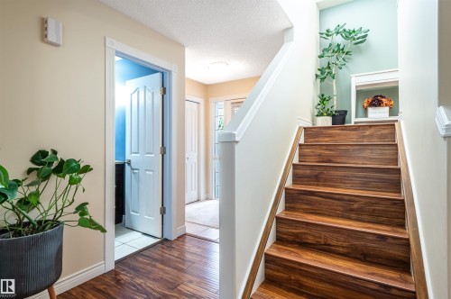 Hardwood-look flooring, staircase with wood-finish treads, white painted trim, and a partially visible doorway to a separate area - 38 Dubonnet Way, St. Albert, AB 