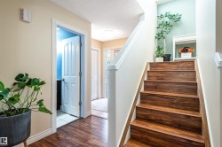 Hardwood-look flooring, staircase with wood-finish treads, white painted trim, and a partially visible doorway to a separate area - 