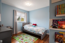 Wood-finish flooring with white baseboards, a window with roller shade and curtain rods, and built-in wall shelving - 