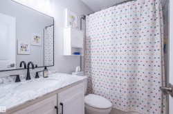 White cabinetry with black hardware, undermount sink, countertop with a marbled finish, matte black faucet, and a large wall-mounted mirror - 