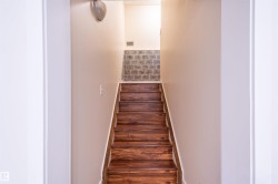 Wood-finish staircase with light wood handrail, neutral wall tones, and tiled wall detail - 