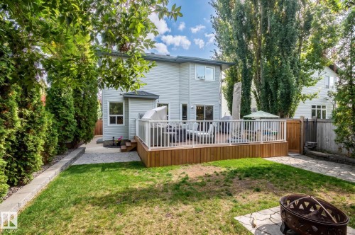 Rear exterior featuring a wood deck with white railings, light-colored siding, a stone pathway, and mature perimeter trees - 38 Dubonnet Way, St. Albert, AB 
