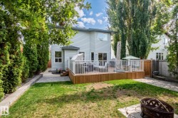 Rear exterior featuring a wood deck with white railings, light-colored siding, a stone pathway, and mature perimeter trees - 