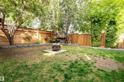 Expansive backyard featuring mature trees, wood privacy fencing, a built-in fire pit area with stone pavers, and concrete retaining walls - 
