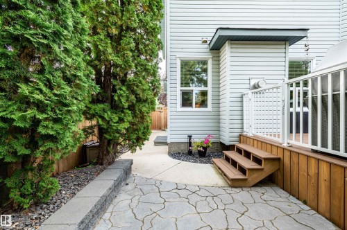 Patio featuring irregular flagstone-style pavers, a raised wood deck with white railings, and mature evergreen trees - 38 Dubonnet Way, St. Albert, AB 