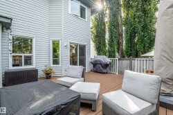 Expansive multi-level wood-finish deck with white railings, featuring direct access via a glass sliding door, and privacy provided by tall mature trees - 