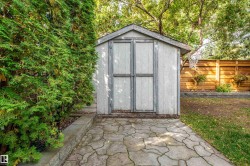 Storage shed with a pitched roof, double doors, and an adjacent paver patio - 