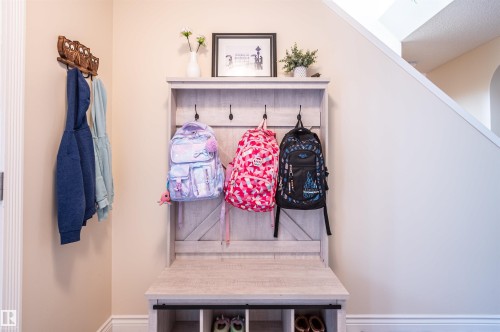 Built-in entryway bench with integrated storage and hooks, featuring a light wood-finish and visible staircase - 38 Dubonnet Way, St. Albert, AB 